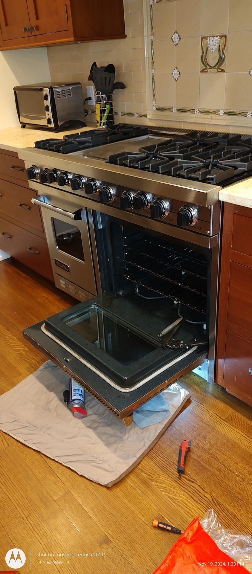 Open oven door in a kitchen with tools and a can on the floor in front of it.